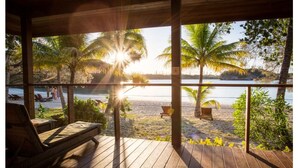 Um deck de madeira com cadeiras de descanso com vista para uma praia e palmeiras.