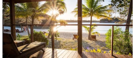 Una terraza de madera con sillones de descanso con vistas a una playa y palmeras.