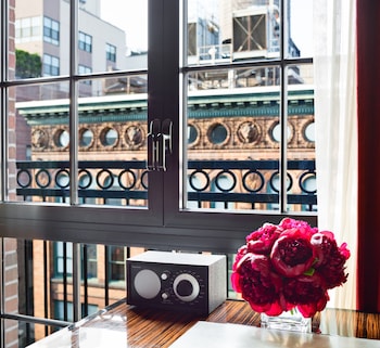 A hotel room with a bed, desk, and chair, a balcony with a table and chairs, and a view of buildings. at Walker Hotel Greenwich Village