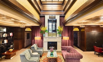 Een ruime lobby met een open haard, twee fauteuils, een bank, een salontafel en een boekenkast.