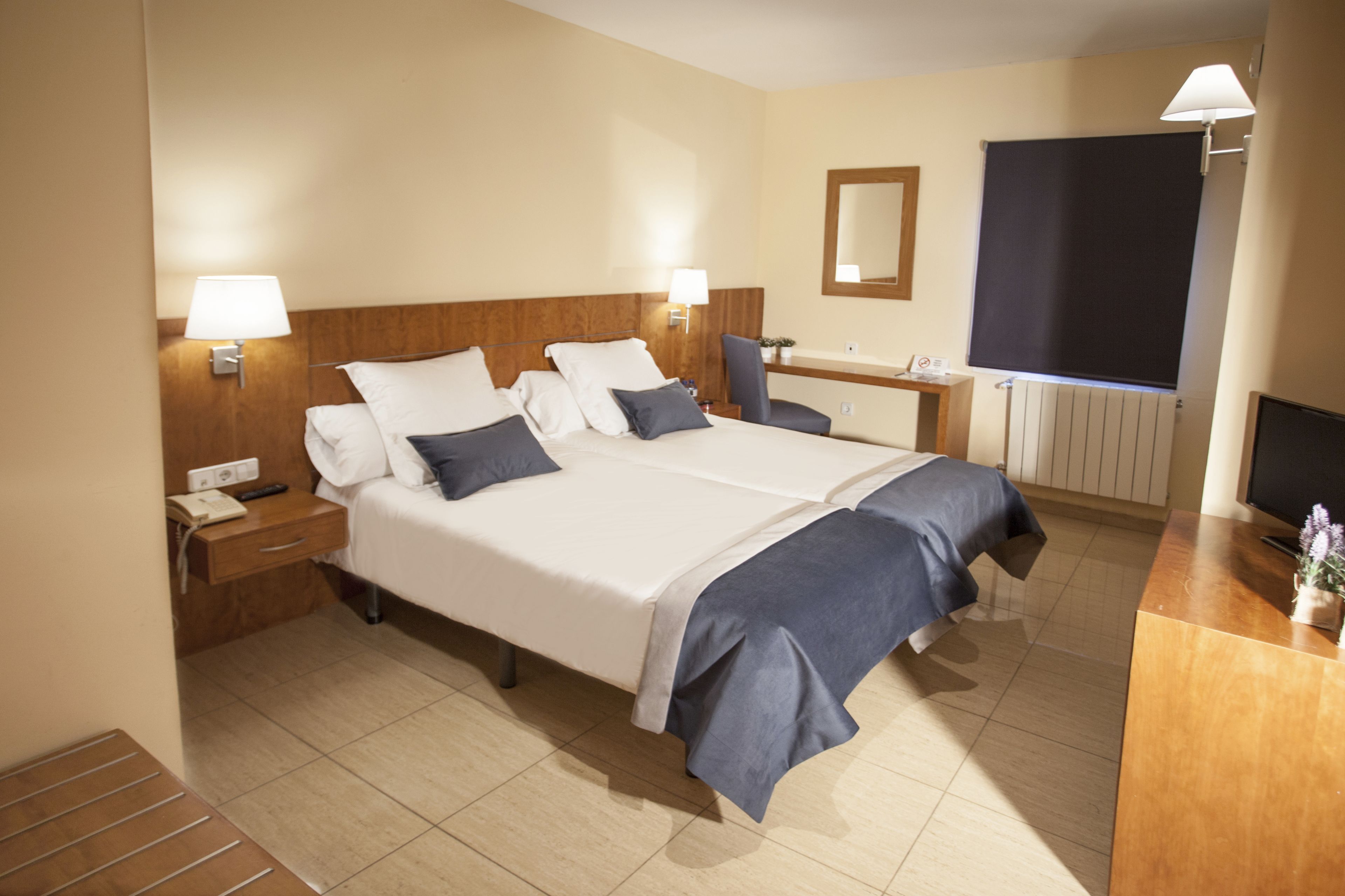A hotel room with two beds, a desk, a chair, a mirror, and a TV.