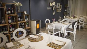 Interior de restaurante com mesas preparadas para refeições, garrafas de vinho em estantes e quadros nas paredes.