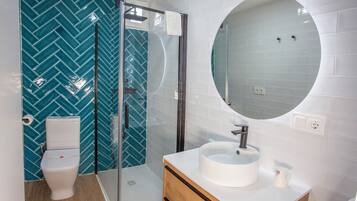Un baño moderno con inodoro, ducha con mampara de vidrio y lavamanos con espejo.