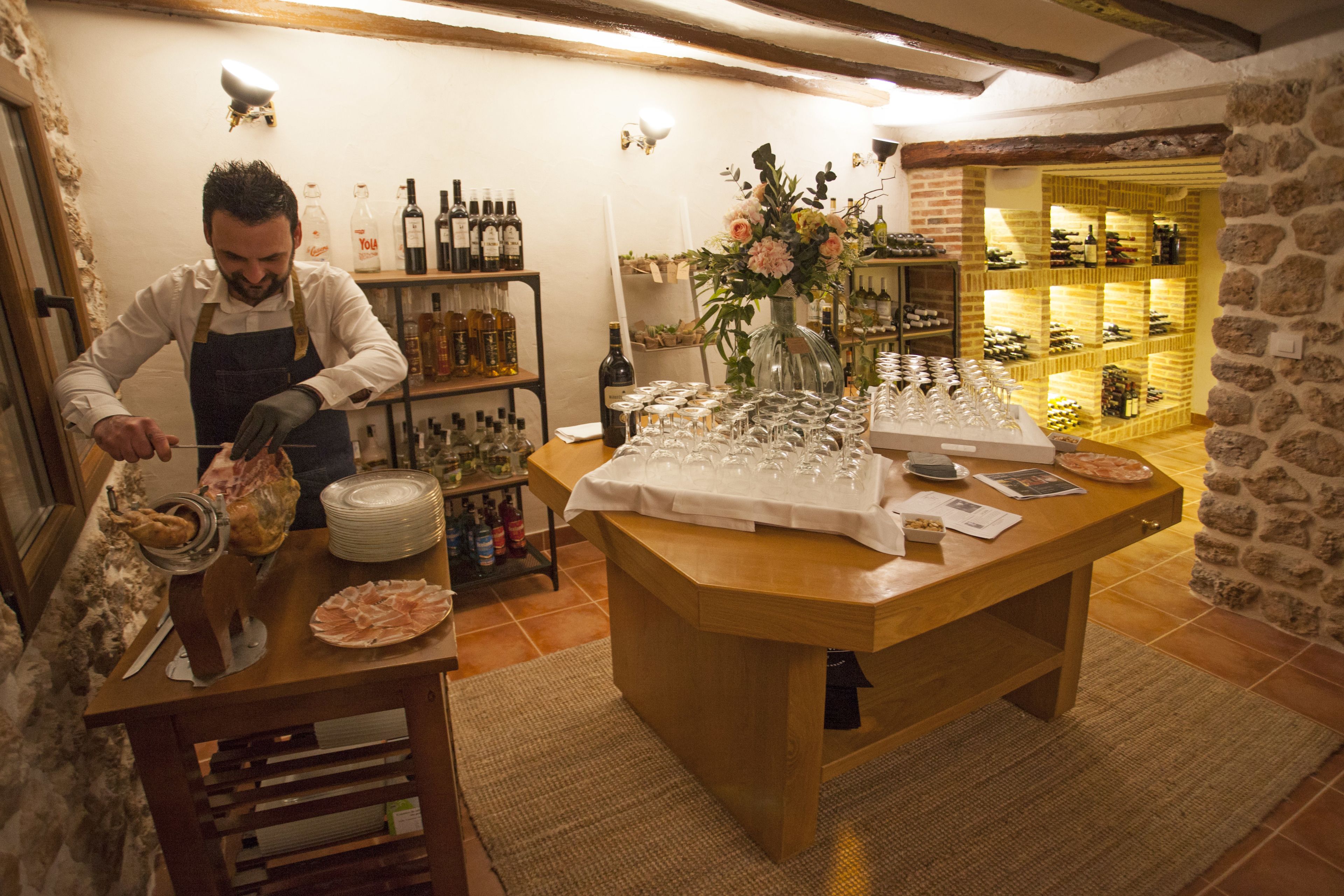 A restaurant with a wooden table set for a meal, surrounded by wine bottles and glasses.