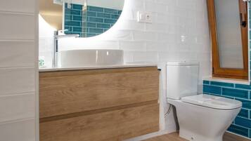 Un baño moderno con tocador de madera, lavabo blanco y espejo redondo.