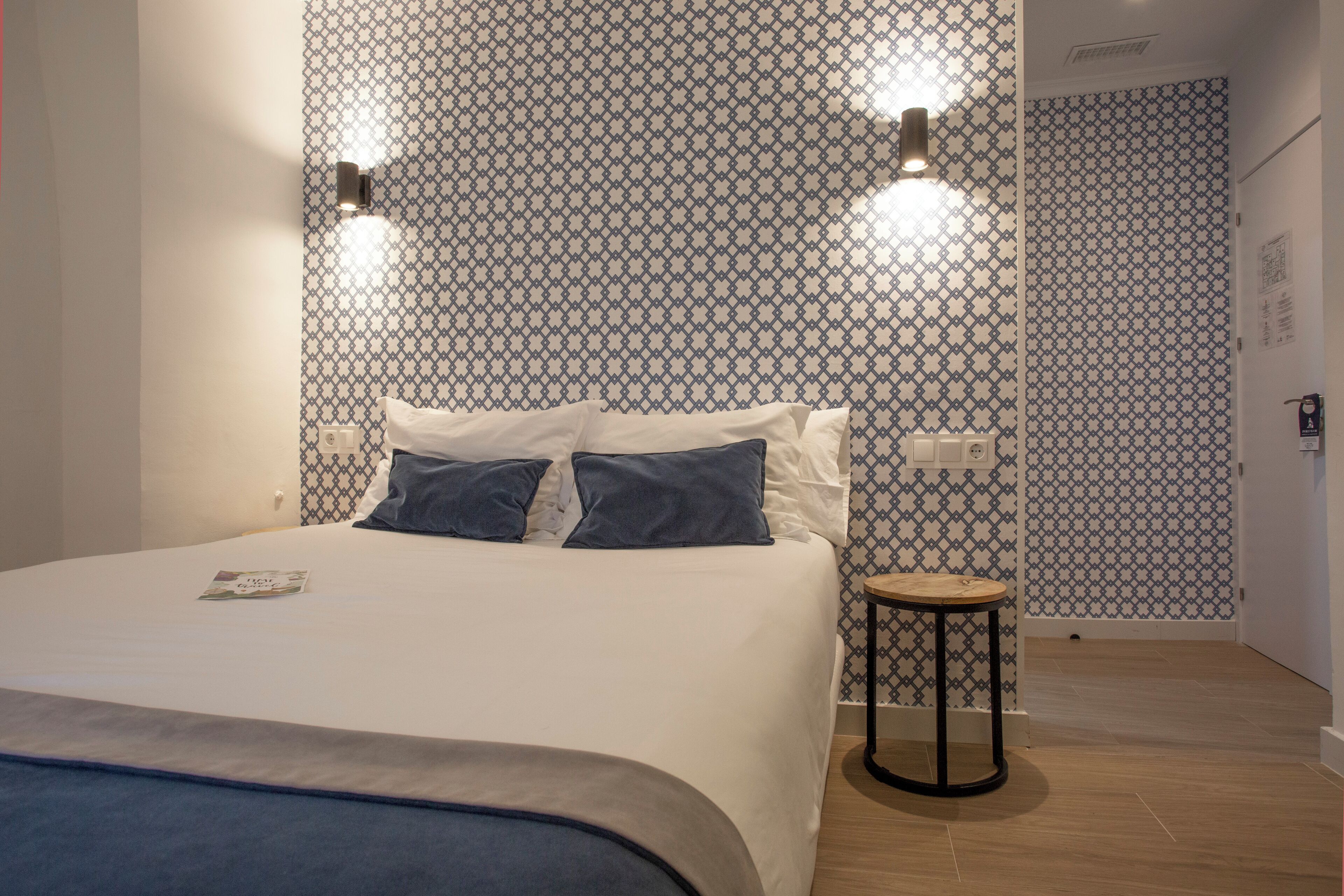 A modern hotel room with a neatly made bed, a small round table, and patterned wallpaper.
