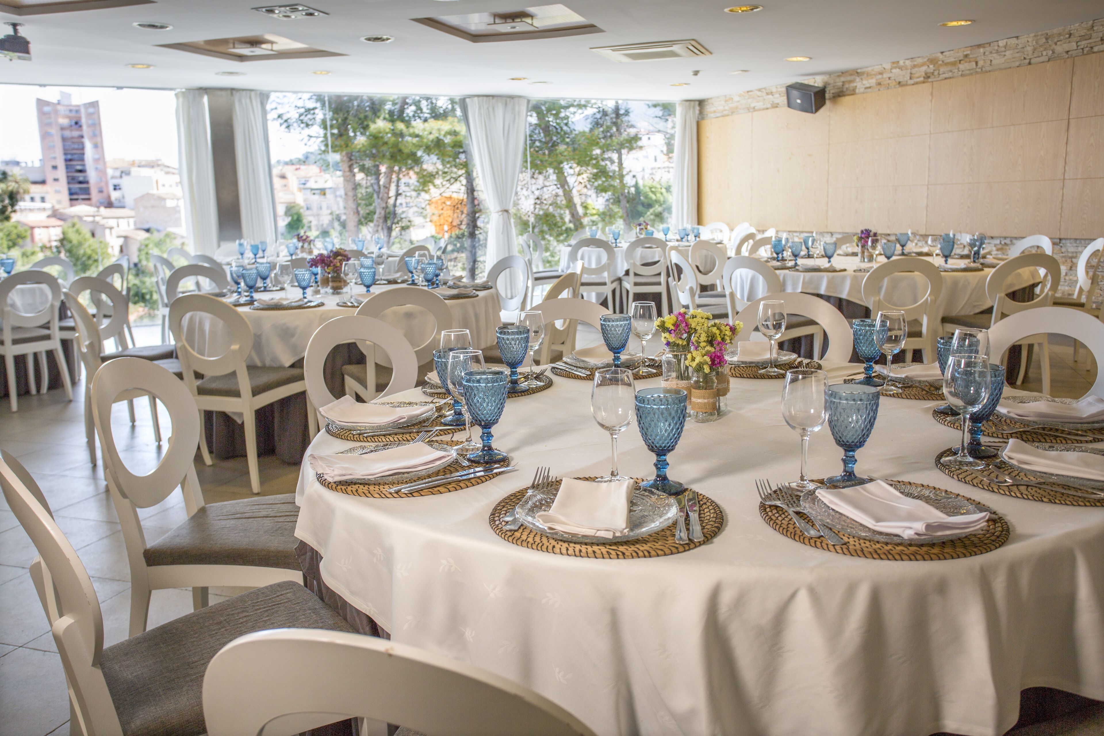 A restaurant with round tables set for dining, featuring blue glassware and white chairs.