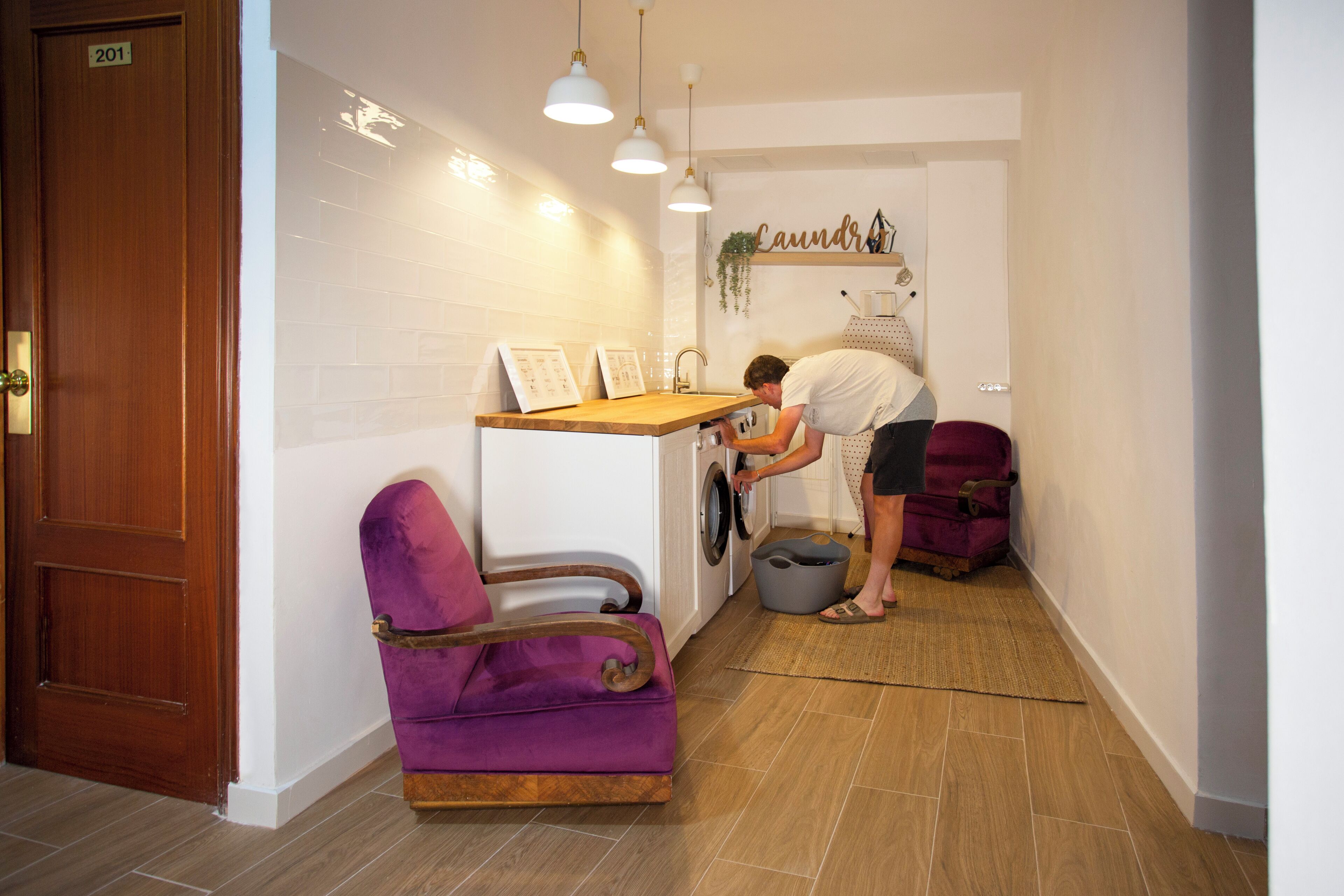 Un área de lavandería con lavadora, una silla morada y un mostrador de madera con un letrero encima.