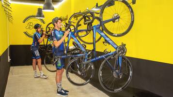 A cycling studio with two cyclists working on bicycles, a yellow and black wall, and a ceiling-mounted bike rack.