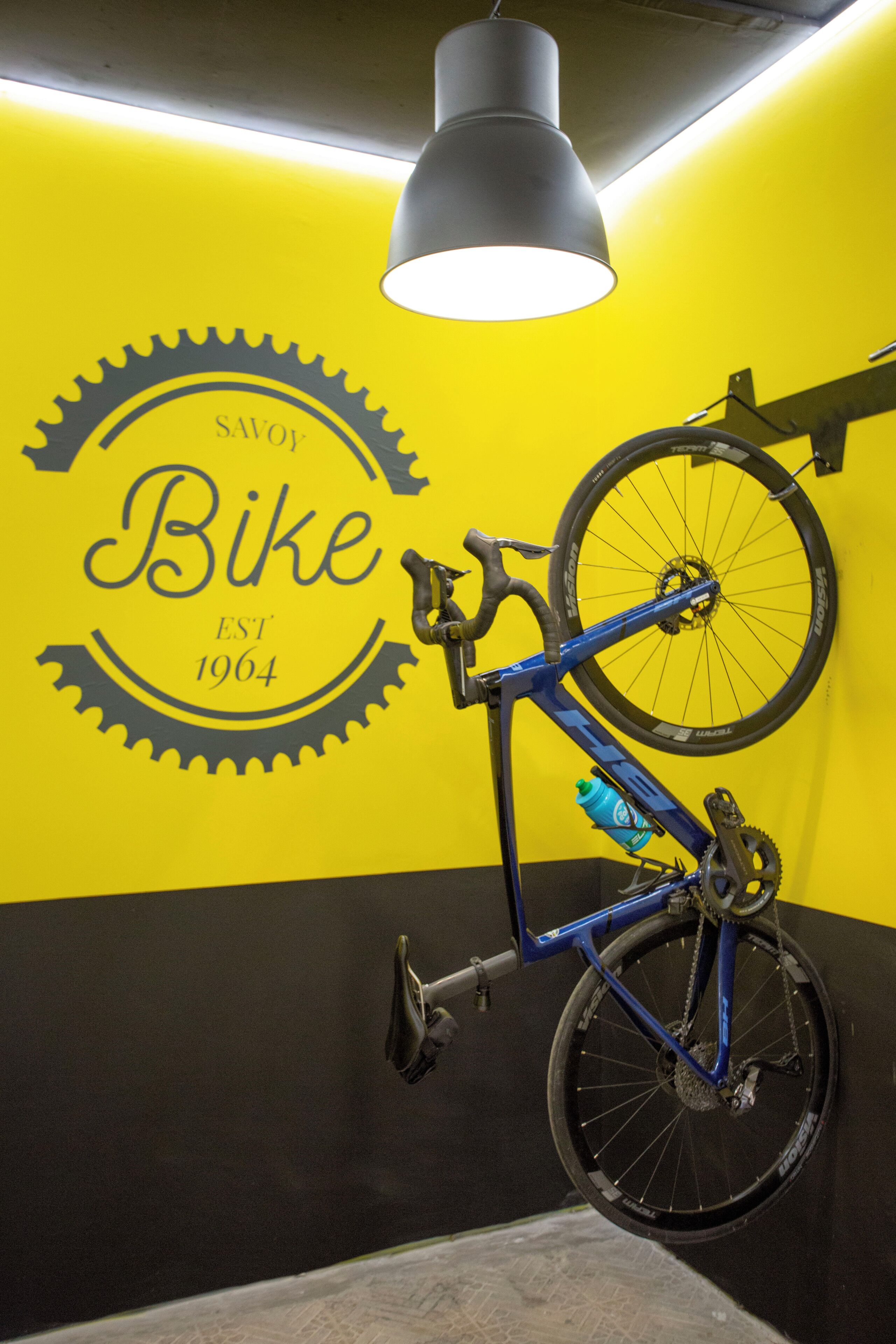 Una bicicleta apoyada contra una pared con un logotipo en forma de engranaje y la inscripción "SAVOY Bike EST 1964".
