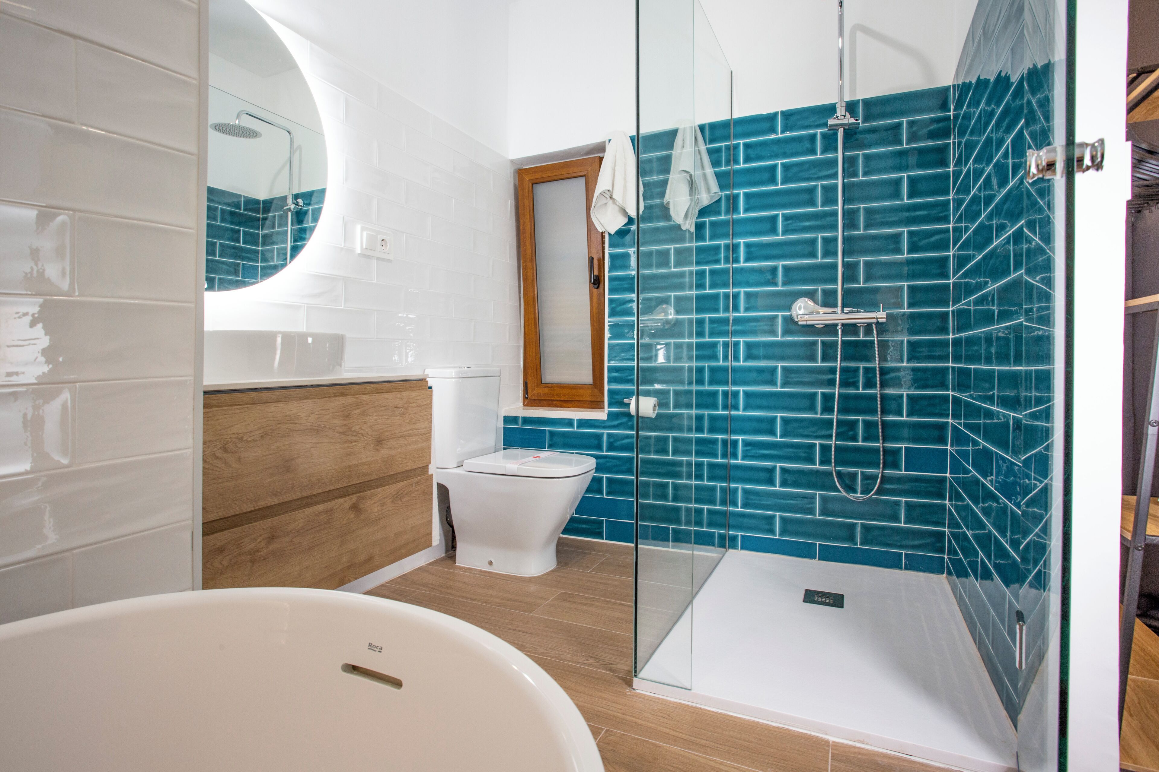 A modern bathroom with a glass-enclosed shower, a white bathtub, and a wooden vanity.