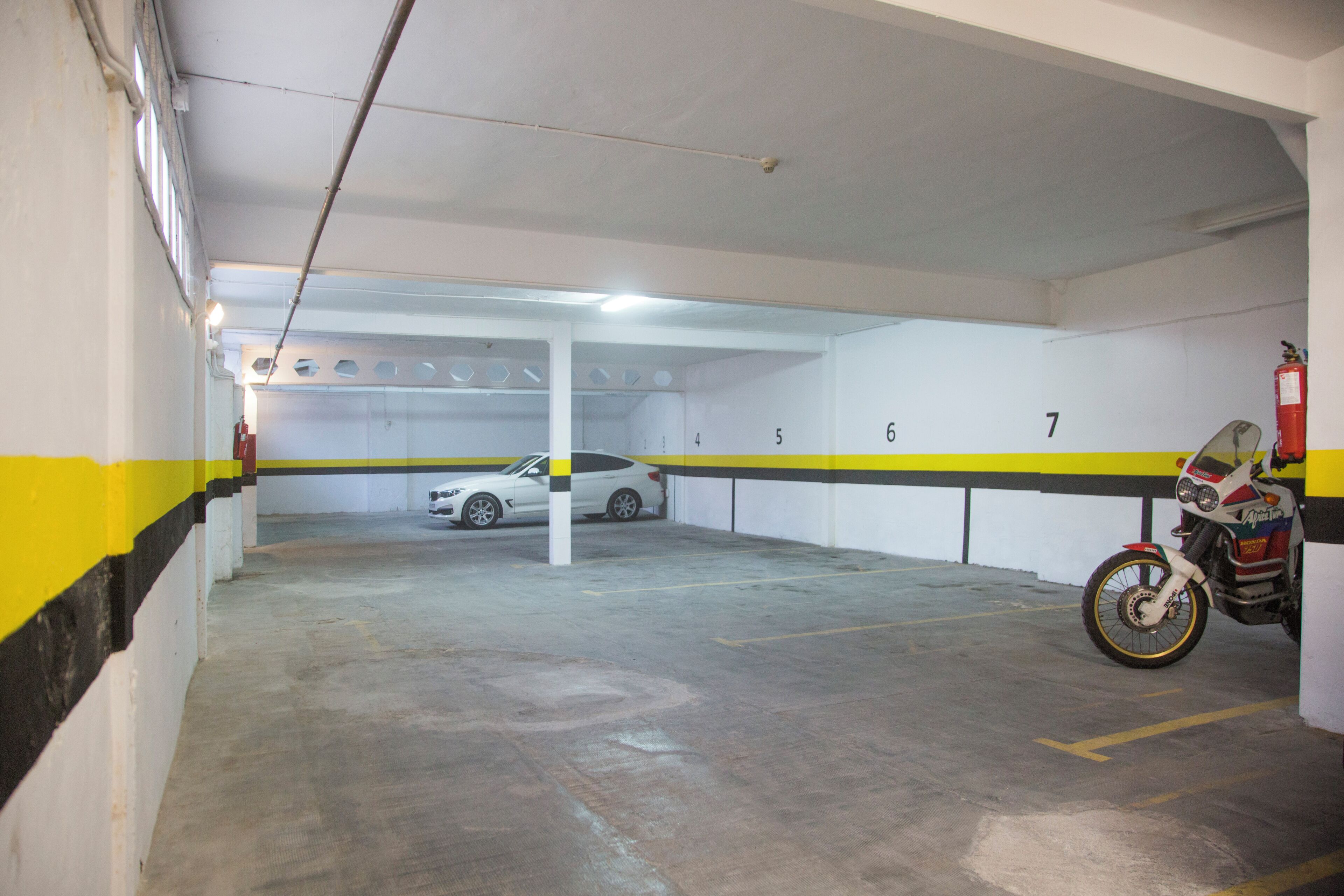 Un estacionamiento con espacios numerados y una motocicleta estacionada en uno de ellos.