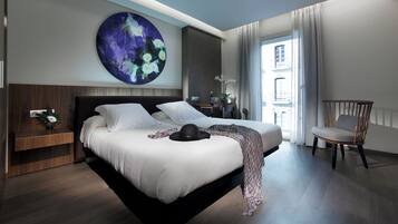 A modern hotel room with a large bed, a nightstand, a chair, and a large abstract painting on the wall.