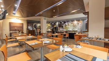 Un comedor moderno con varias mesas y sillas, una cocina al fondo y un techo de madera.