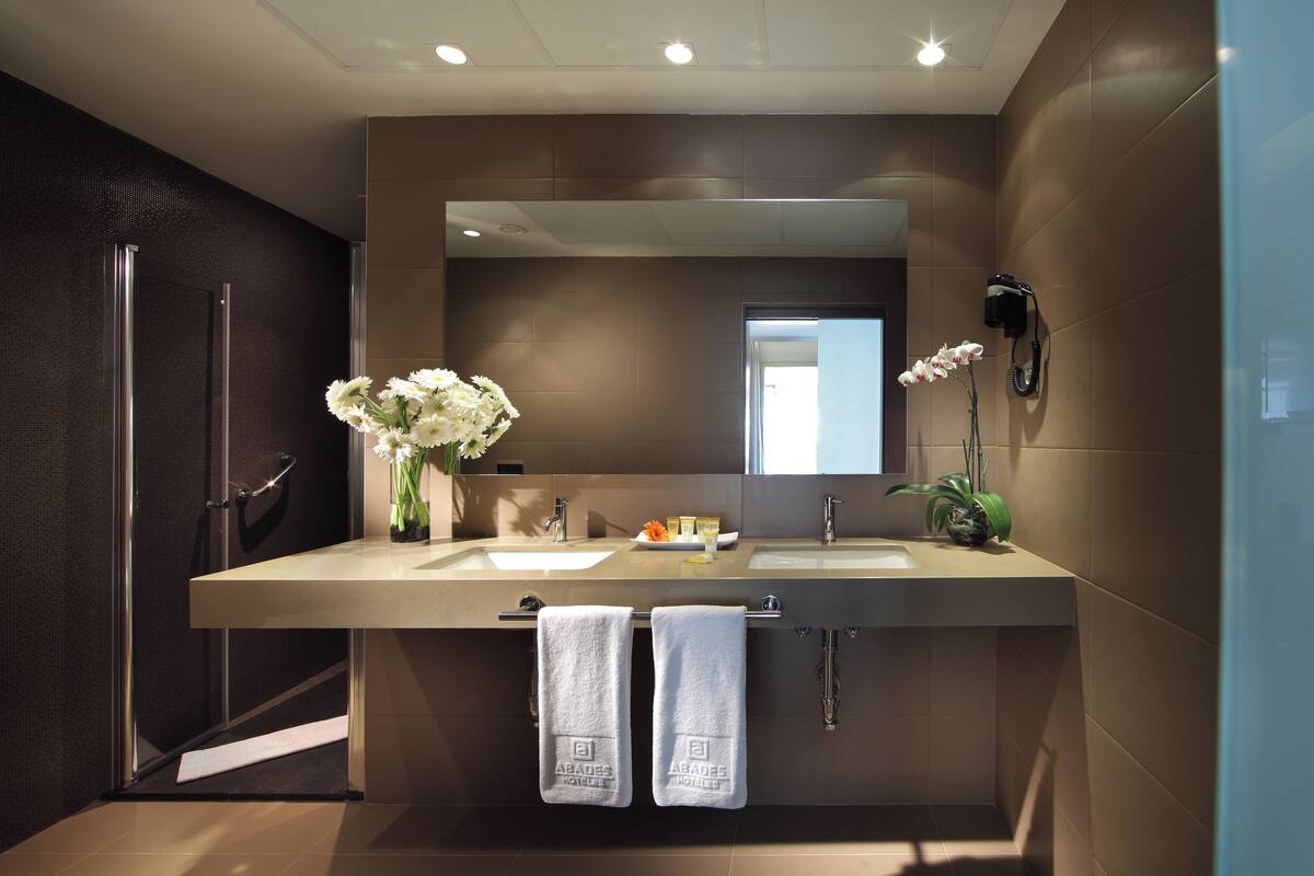 A modern bathroom with two sinks, a large mirror, and a shower area.