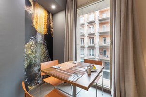 Un comedor con una mesa dispuesta para dos personas, vista a un edificio con balcones y un mural en la pared.