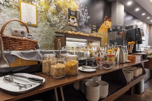 Montaje de bufé con diferentes opciones de comida, una máquina de café y un letrero que indica las opciones de desayuno.