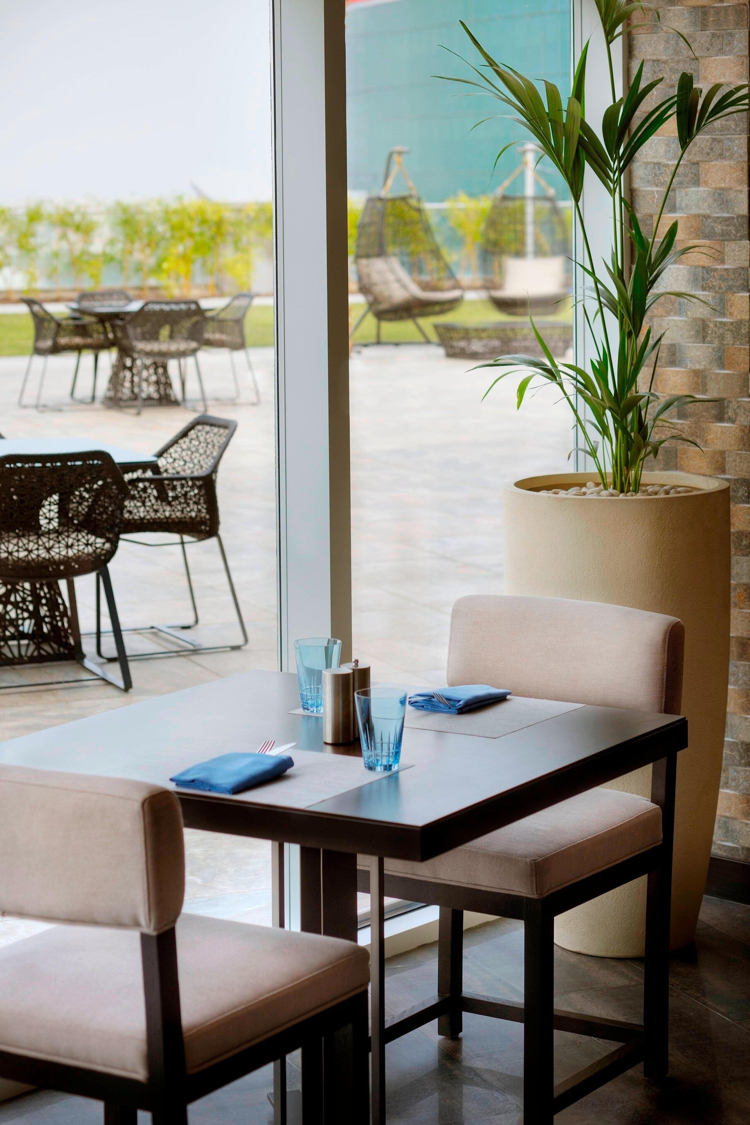 Comedor con mesa dispuesta para dos, una planta grande en maceta y vistas del área de asientos al aire libre.