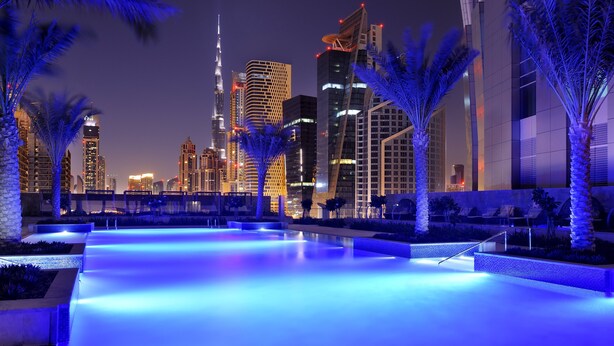 A nighttime view of a modern cityscape with illuminated buildings and a pool area. - JW Marriott Marquis Hotel Dubai (Dubai)