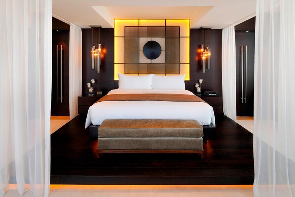 Una habitación de hotel moderna con una cama grande, un banco, una lámpara de pared y un panel decorativo.