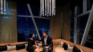 A modern interior with a large window overlooking a cityscape at night, featuring a sofa and a small table with a glass of wine. - JW Marriott Marquis Hotel Dubai (Dubai)