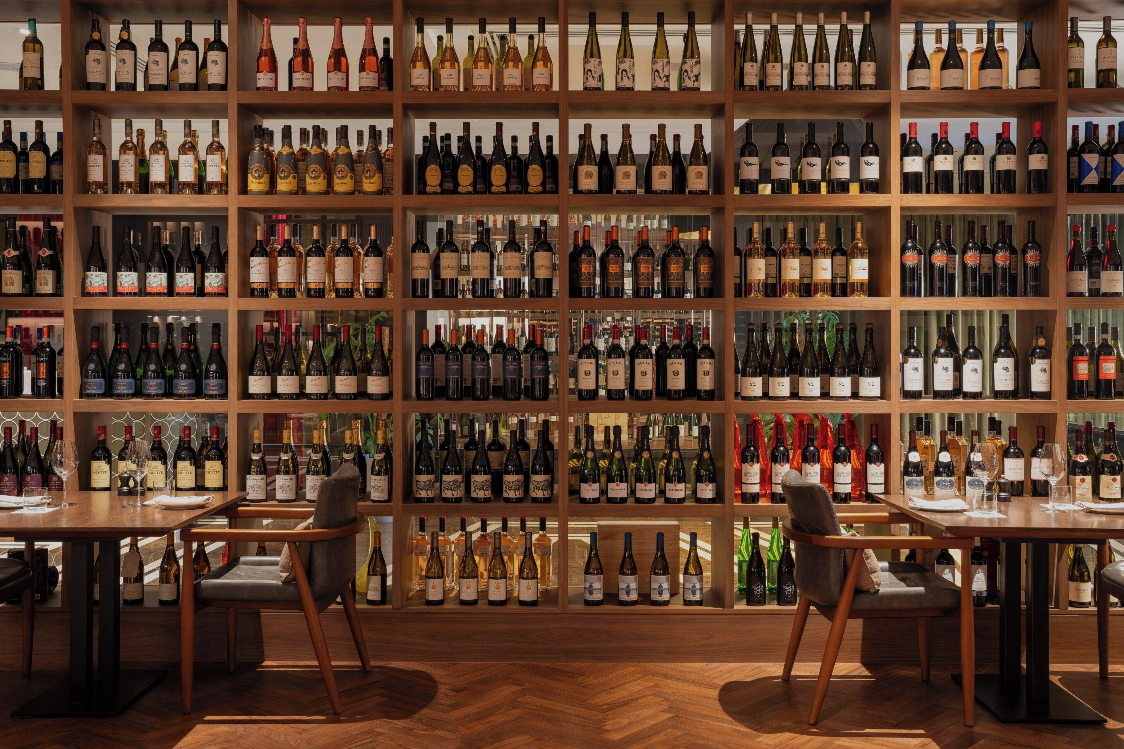 A wine cellar with shelves of wine bottles, wooden tables, and chairs.