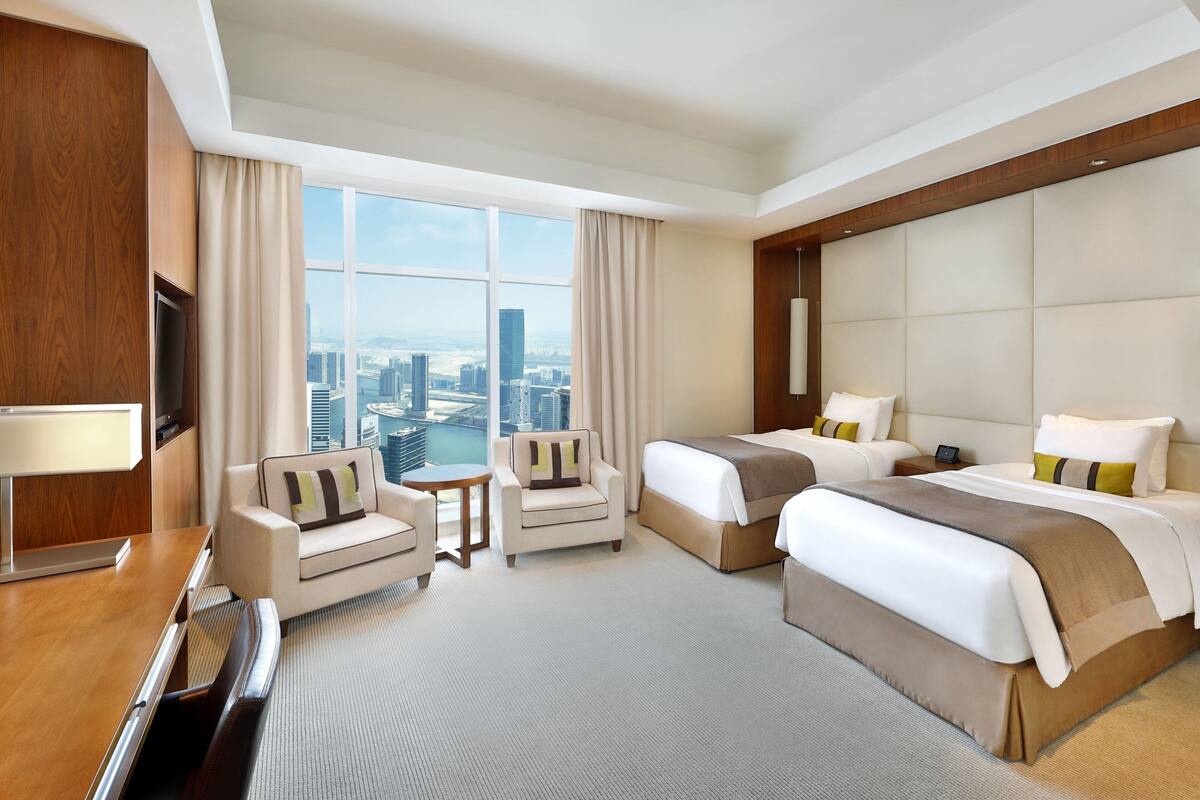 A hotel room with two beds, a sofa, a TV, and a city view.