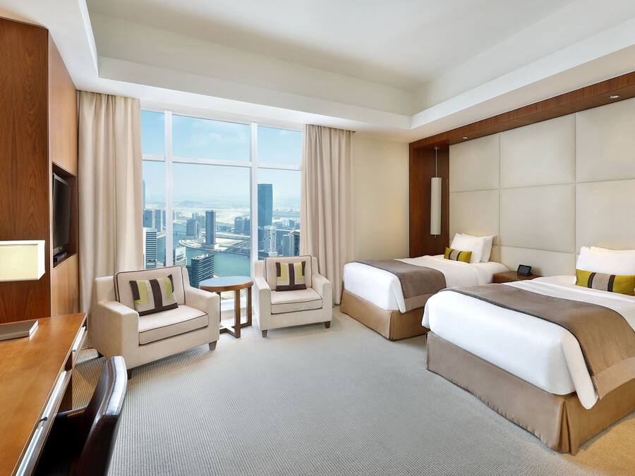 Habitación de hotel con dos camas, un sofá, televisión y vista a la ciudad.