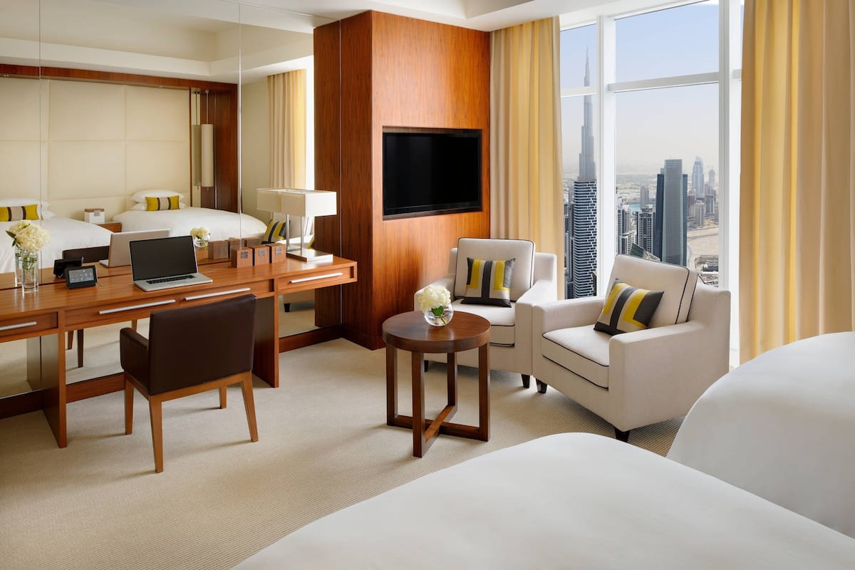 A hotel room with a large bed, a desk with a laptop, a TV mounted on the wall, and a view of the city skyline.