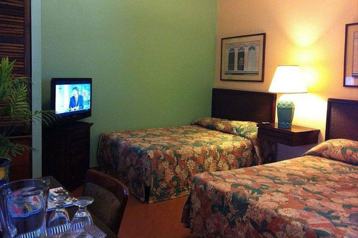 A hotel room with two beds, a television, a lamp, and a small table with glasses.
