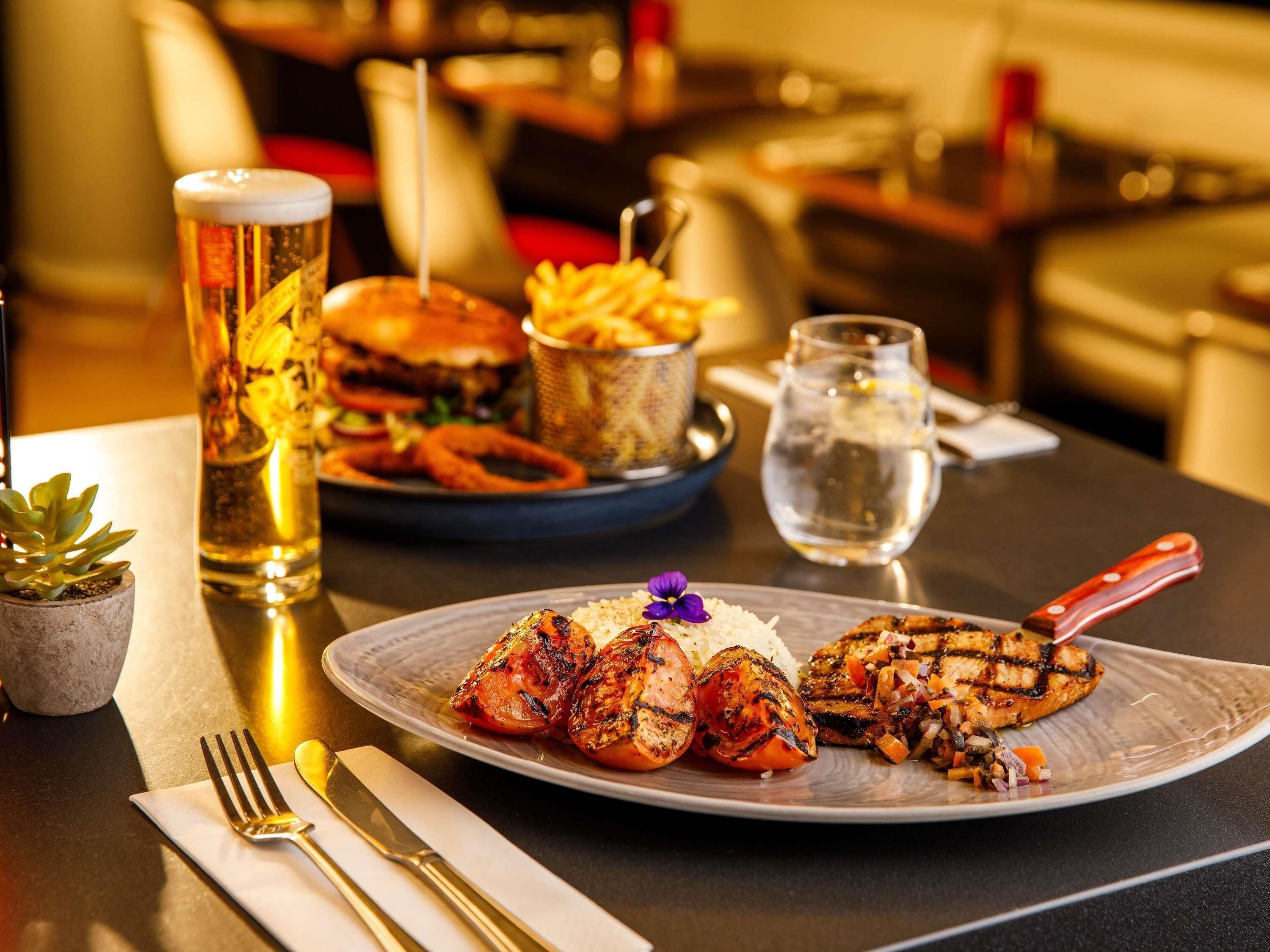 A dining table with a plate of grilled chicken, rice, and vegetables, a burger, and French fries.