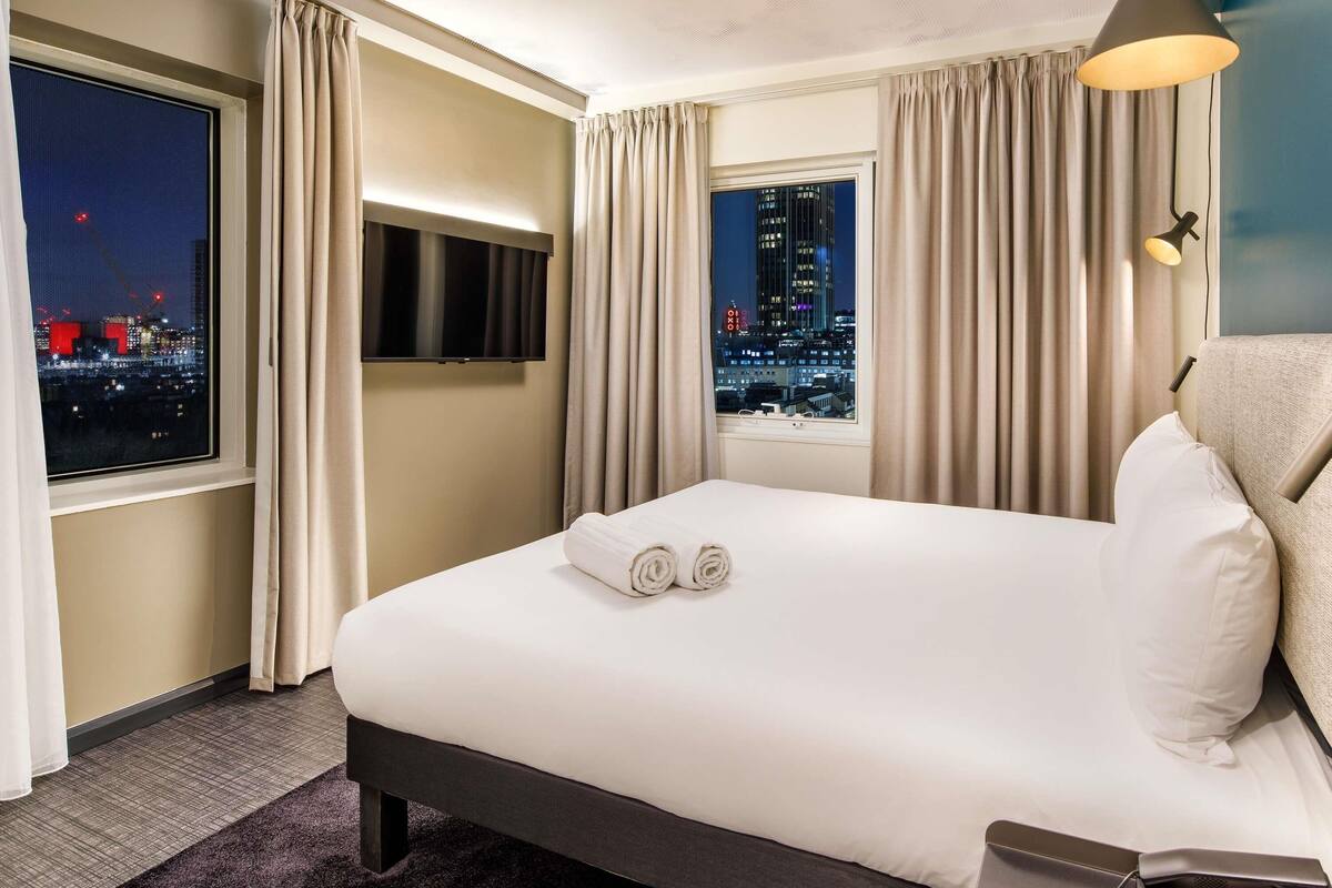 Una camera d'albergo con un letto, una TV, vista sulla città e un telefono sul comodino.