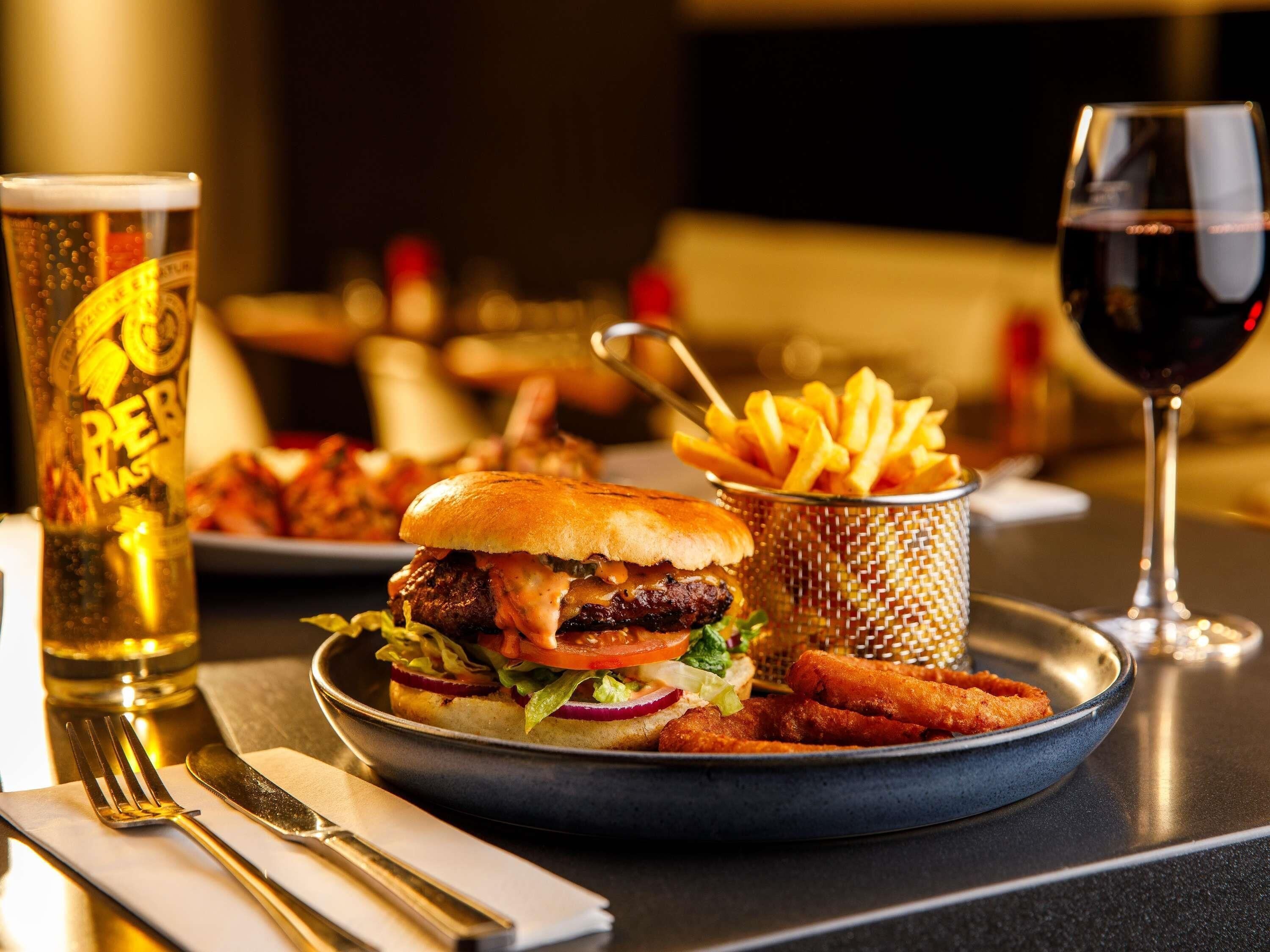 Un repas composé d'un hamburger, de frites et d'un verre de vin rouge, servi sur une table.