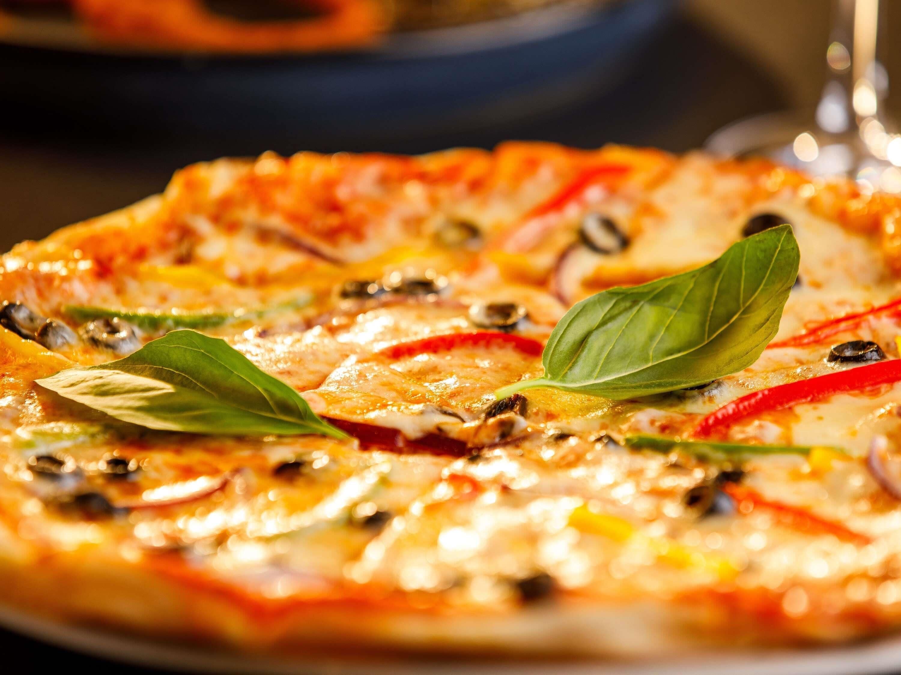 Una pizza con diferentes ingredientes y hojas de albahaca por encima.