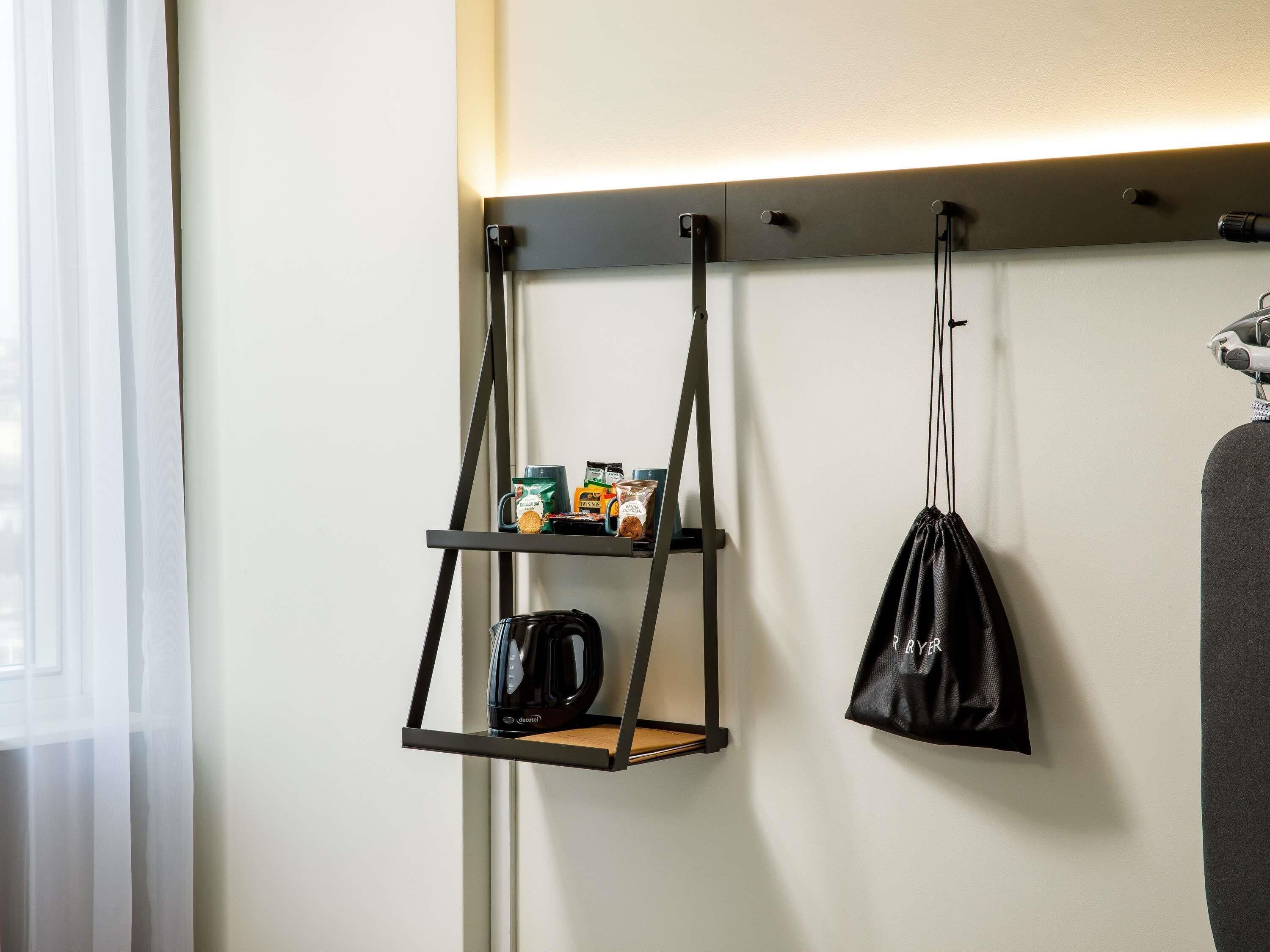 Une étagère murale avec une machine à café et des en-cas, un sac suspendu et un porte-manteau avec une veste.