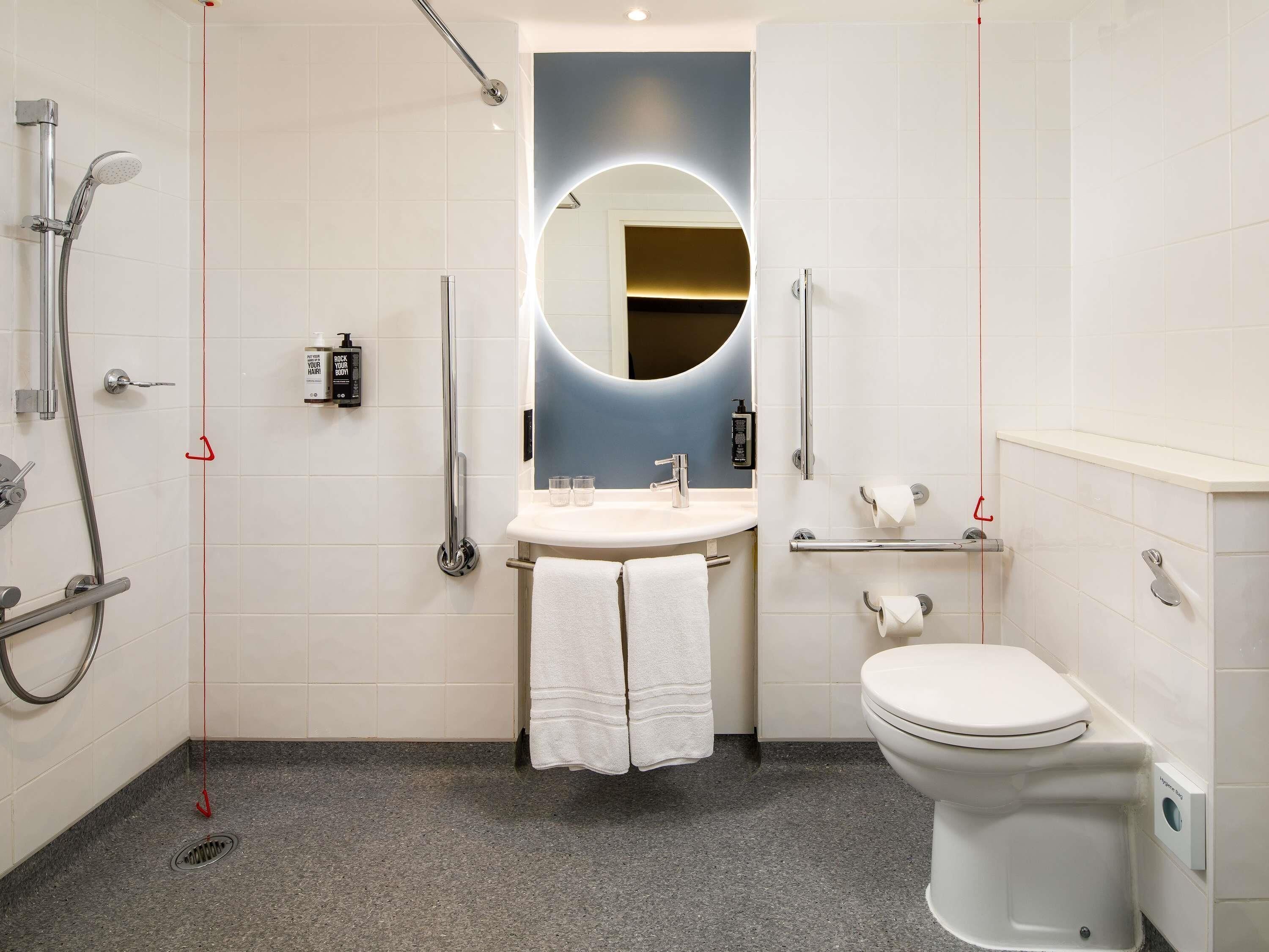 A modern bathroom with a shower, toilet, sink, and a mirror with a circular light.