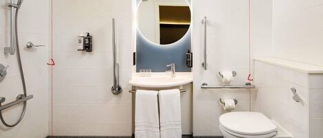 A modern bathroom with a shower, toilet, sink, and a mirror with a circular light.