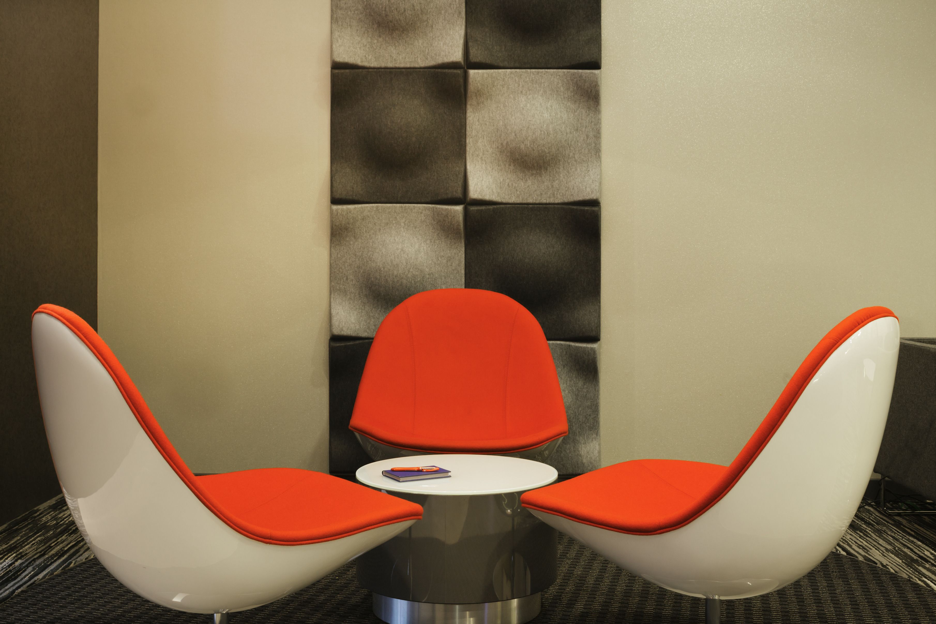 A corner seating area with two white chairs with orange cushions and a small round table.