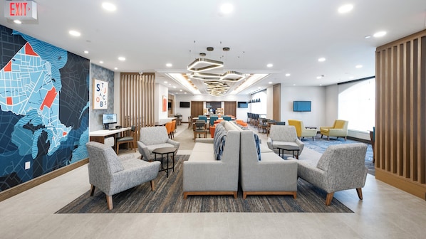 Un hall d’hôtel moderne doté d’une grande fresque représentant une carte, de sièges confortables, d’un espace repas et d’un écran de télévision.