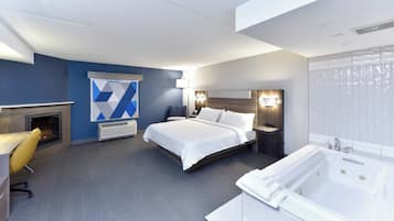 A modern hotel room with a large bed, a fireplace, a sitting area with a yellow chair, a desk, and a bathroom with a bathtub.