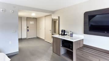 A hotel room with a kitchenette, a flat-screen TV, a coffee maker, and a microwave.