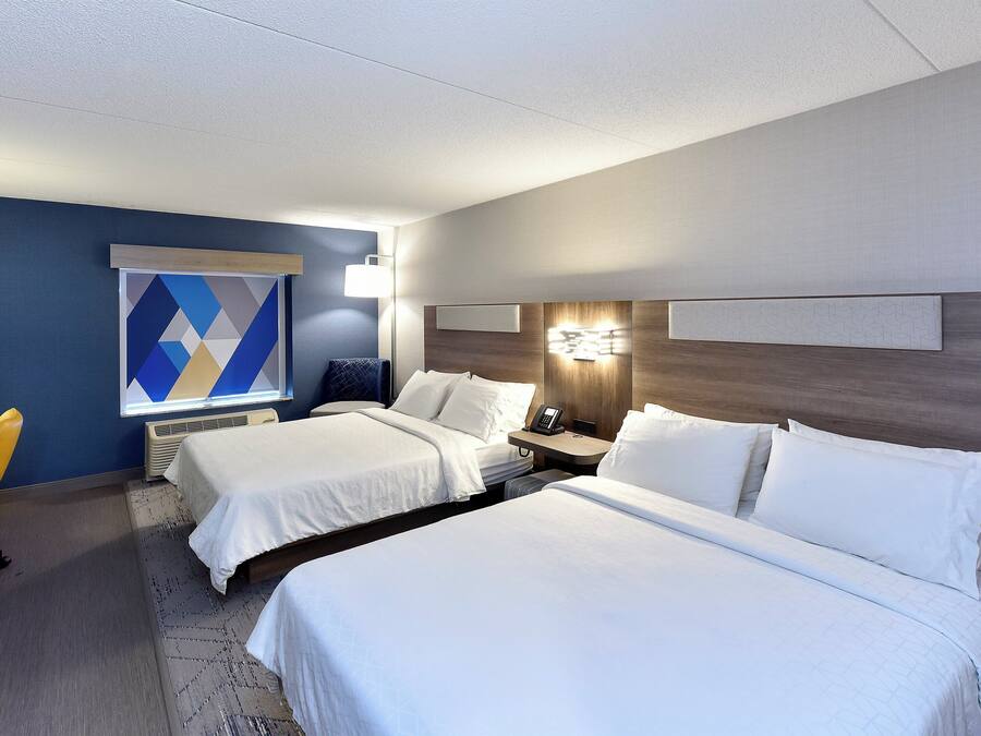 Una habitación de hotel con dos camas, un escritorio con silla, una ventana con persianas y un teléfono en la pared.