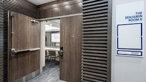 A hotel room with a wooden door, a conference table, and a sign indicating 'The Benjamin Room B' and 'Vacant'.