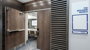 Ein Hotelzimmer mit Holztür, einem Konferenztisch und einem Schild mit der Aufschrift 'The Benjamin Room B' und 'Frei'.