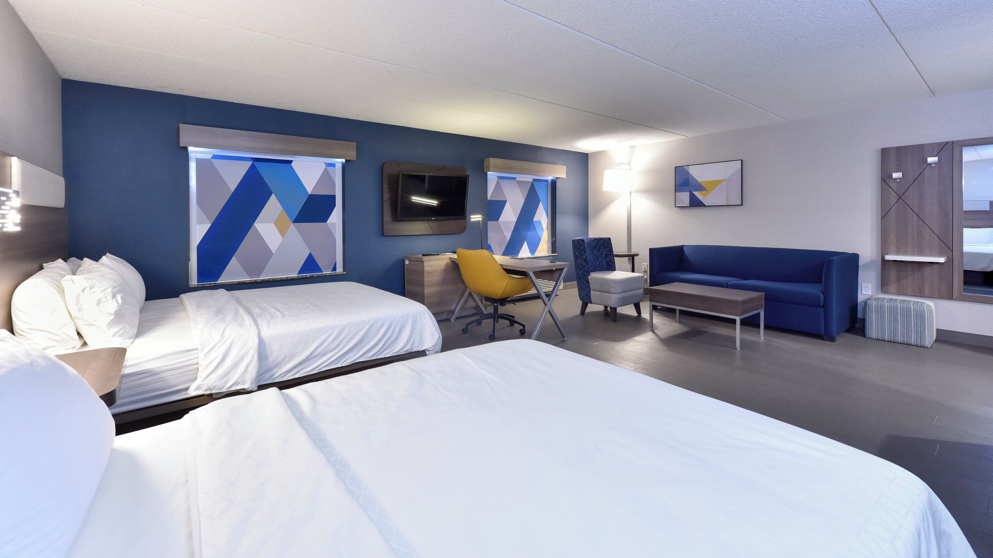 A hotel room with two beds, a desk, a chair, a sofa, and a TV.