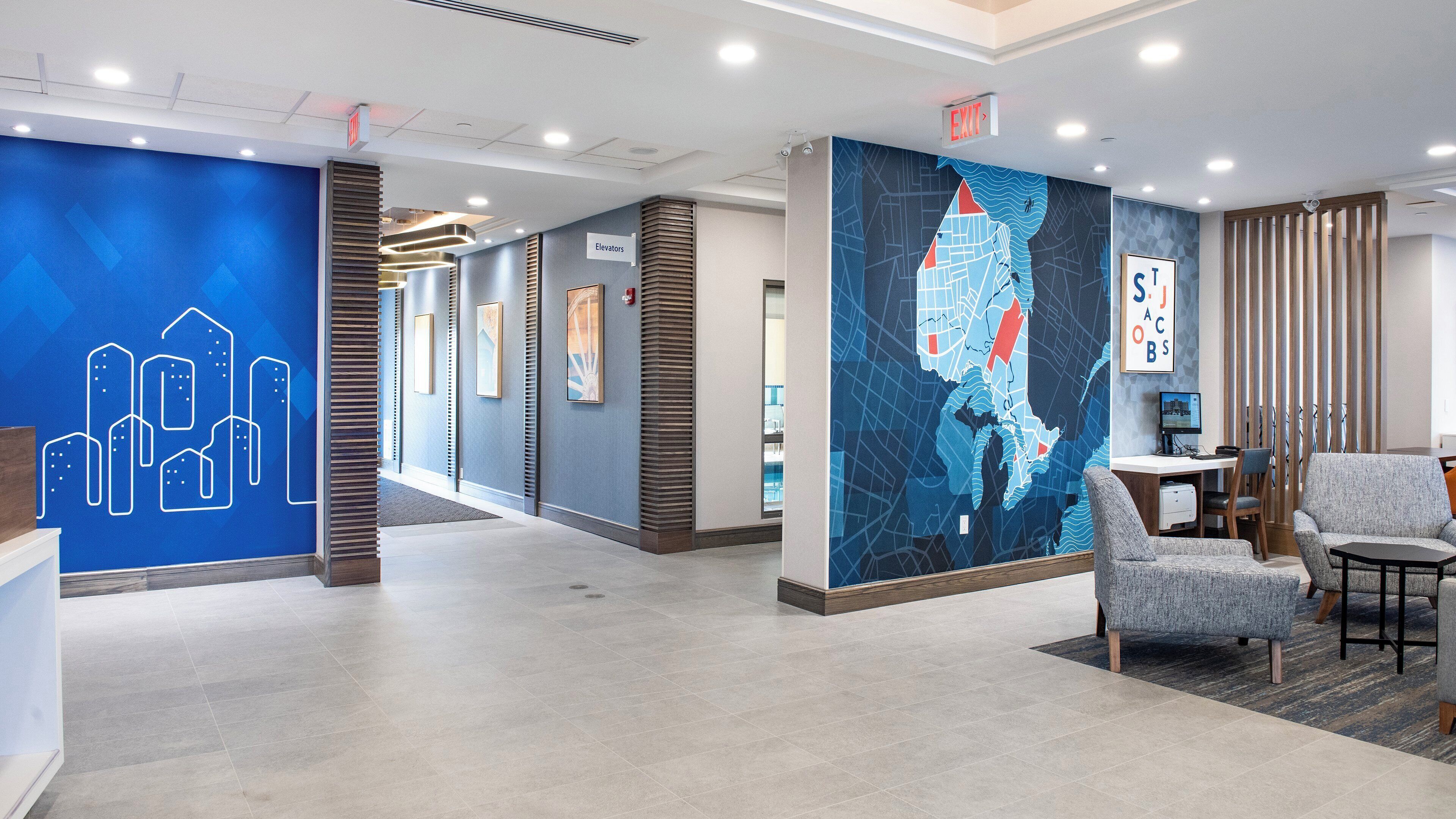 Eine moderne Hotelhalle mit blauer Wand, die ein Stadtbild-Mural zeigt, einem Empfangsschalter und einer Sitzecke mit einer Karten-Mural.