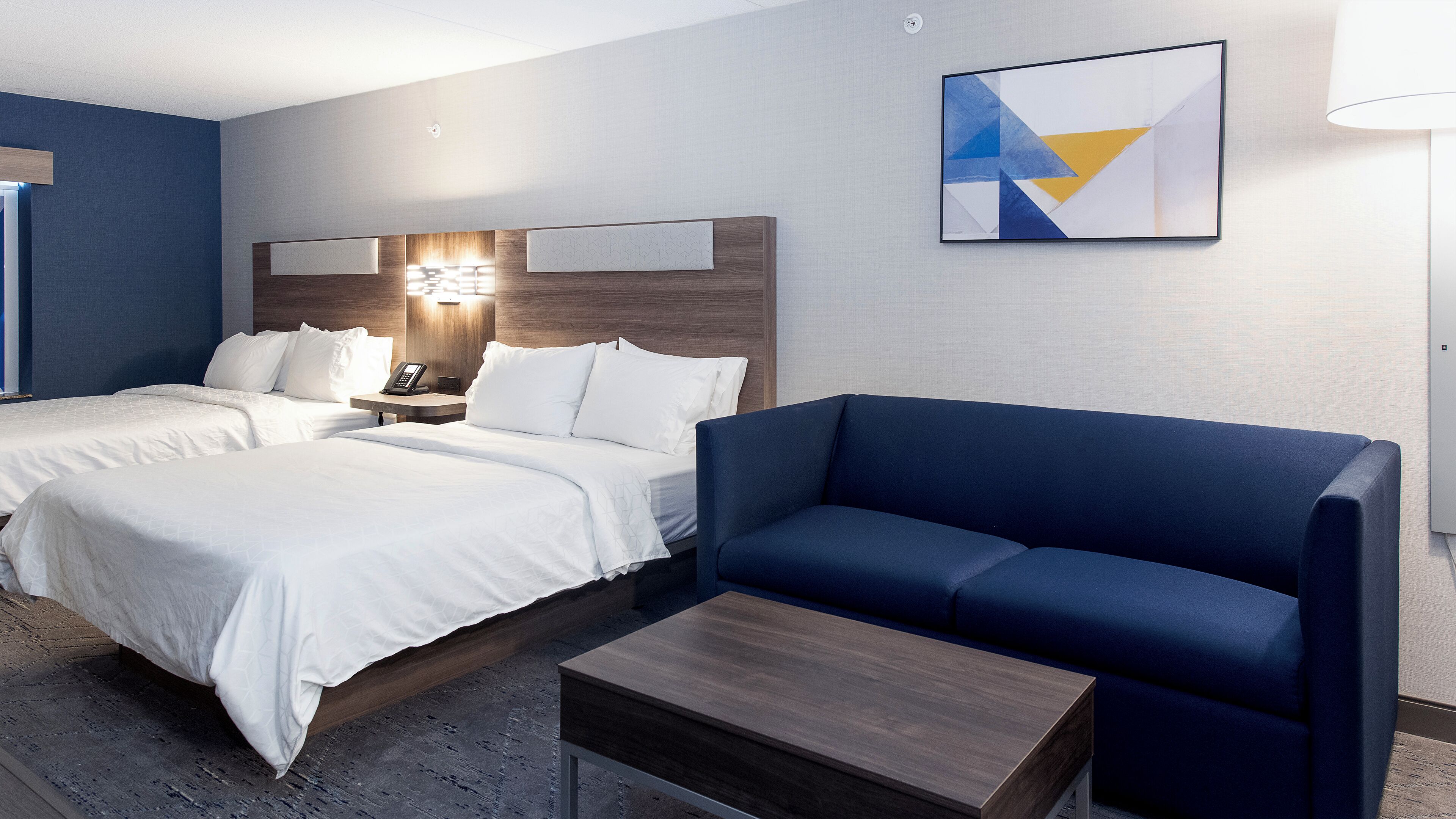A hotel room with two beds, a desk, a chair, and a painting on the wall.