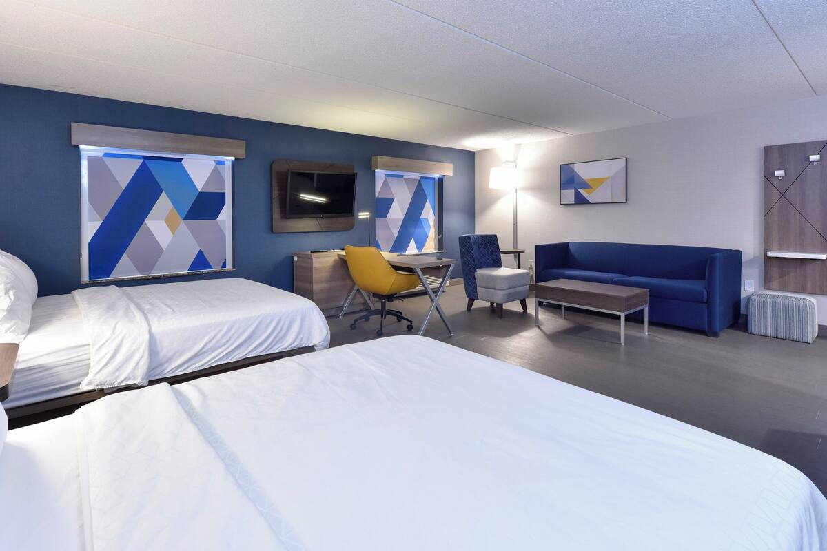 A hotel room with two beds, a desk, a chair, a sofa, and a TV.