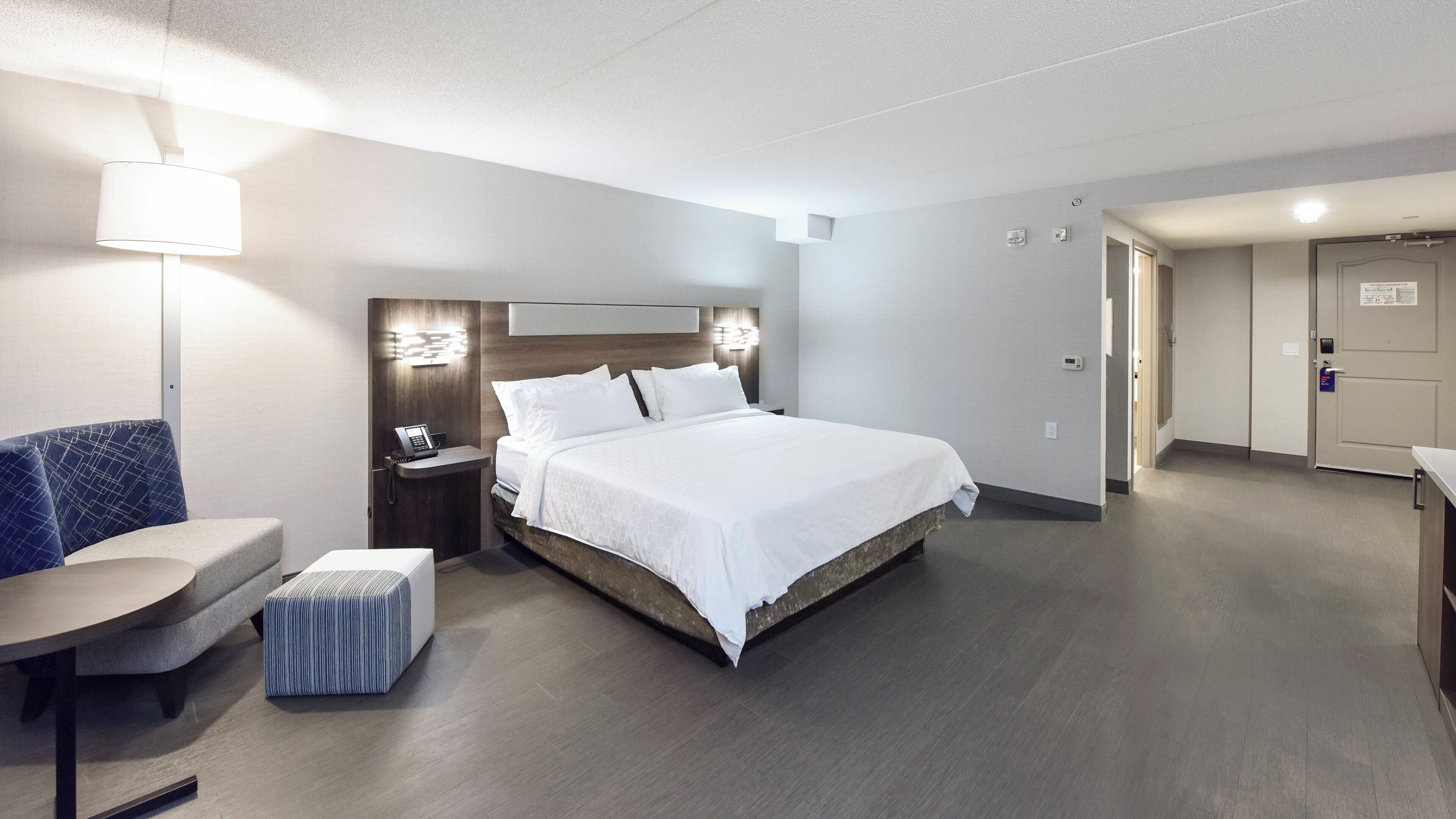 A hotel room with a bed, a desk, a chair, and a small ottoman.