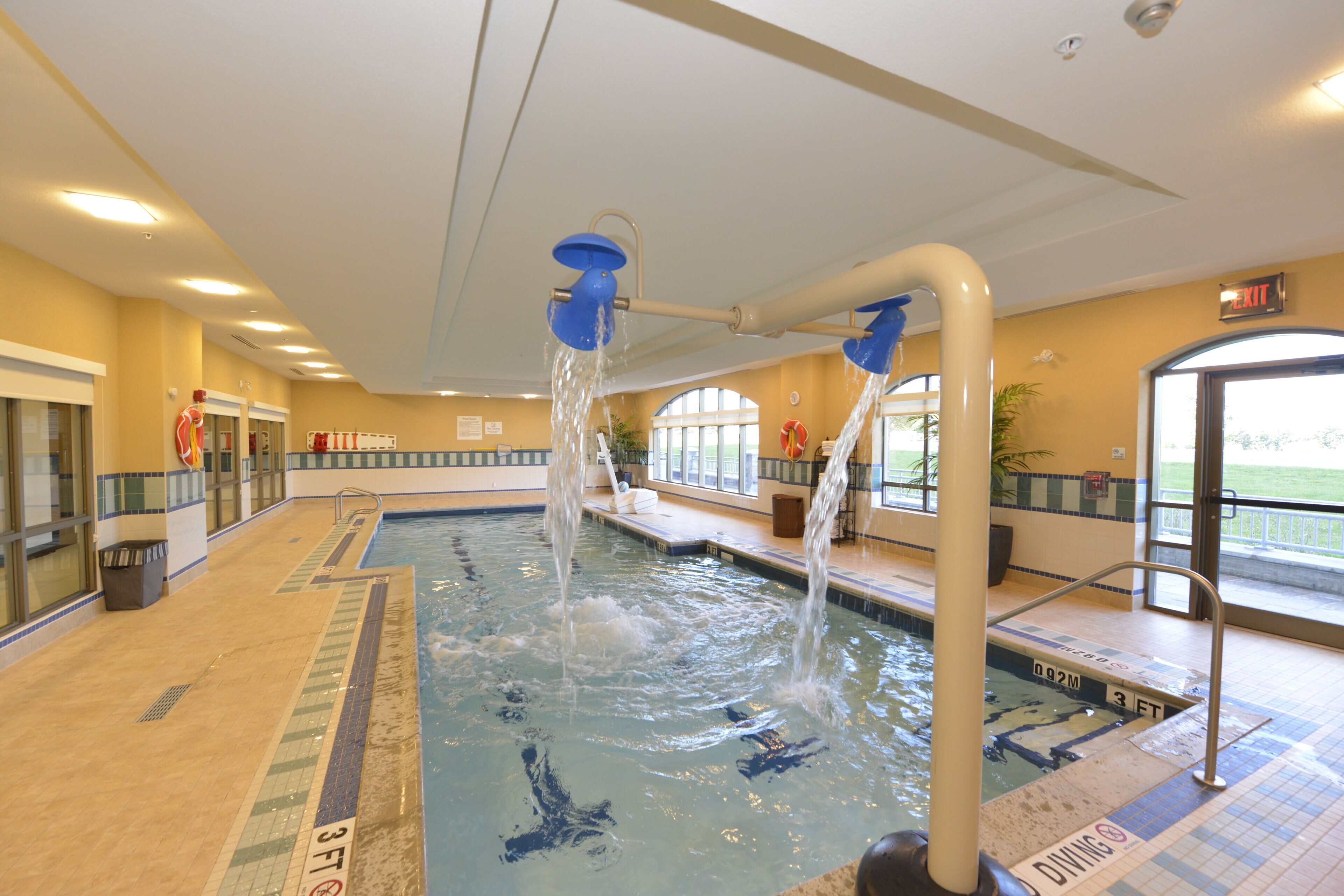 An indoor swimming pool with multiple water jets, clear lane markings, and a diving area.